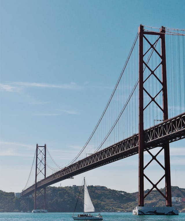 A sailboat sailing under a bridge in Lisbon.